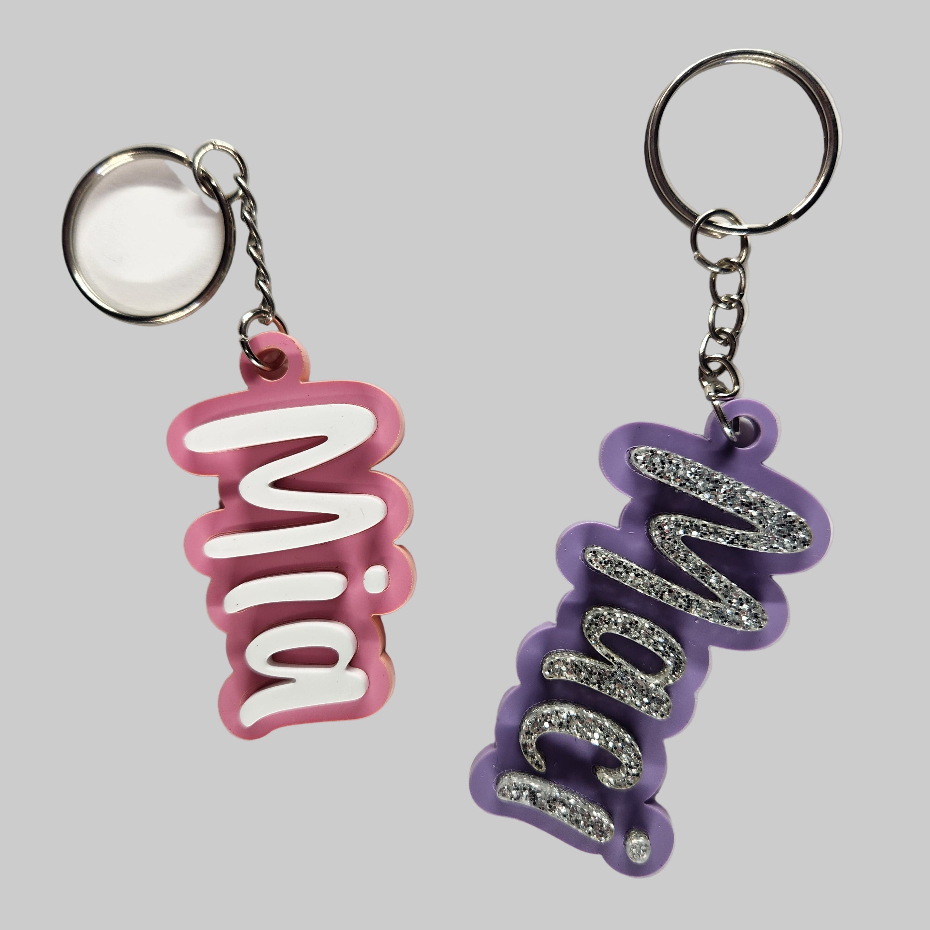 Two acrylic keychains with names personalized in pink and purple colors.